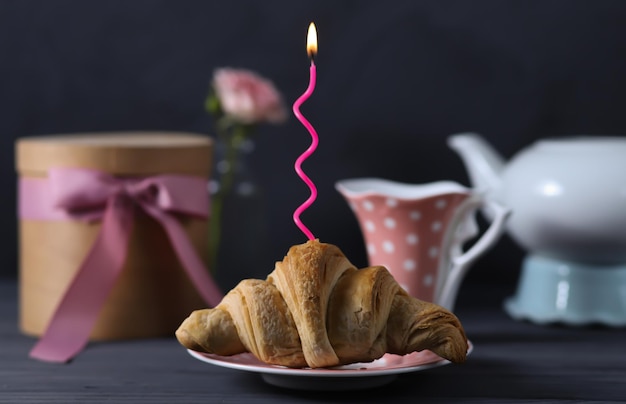 A birthday card featuring a croissant with a festive candle and a cup