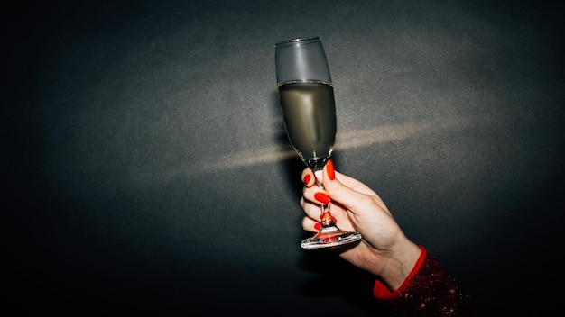 Birthday cheer Holiday party Happy celebration Advertising background Unrecognizable woman red manicure holding champagne glass isolated black light splash copy space