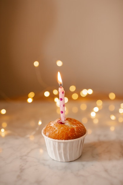 Birthday cup cake with burning candle over glow lights