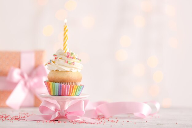 Birthday cupcake with candle on table against blurred lights