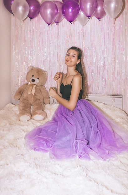 Birthday girl closeup in purple skirt. Young pretty woman is sitting on the bed with purple air balls in her hand