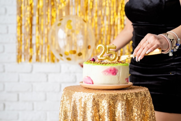 Foto festa di compleanno. bella donna castana in vestito da partito nero che tiene palloncino che festeggia il suo compleanno tagliando la torta