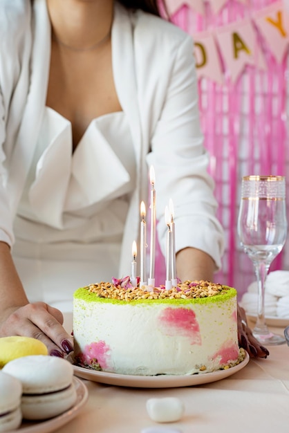 写真 誕生日パーティー誕生日テーブル白いパーティー服を着た魅力的な女性がケーキケーキポップマカロンやその他のお菓子で誕生日テーブルを準備します