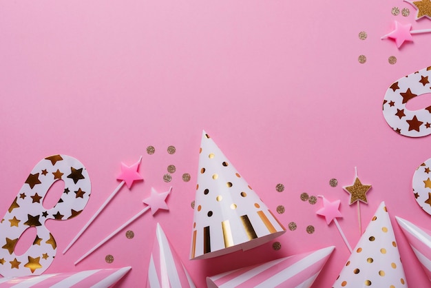 Birthday party concept. Party hats, masks and birthday candles on the pink background. Top down view with copy space