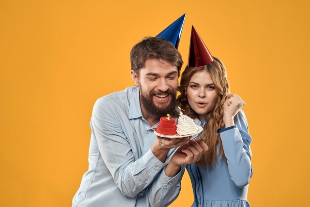 Birthday party man and woman in a cap with a cake on a yellow background cropped view person