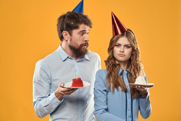 Birthday party man and woman in a cap with a cake on a yellow background cropped view person