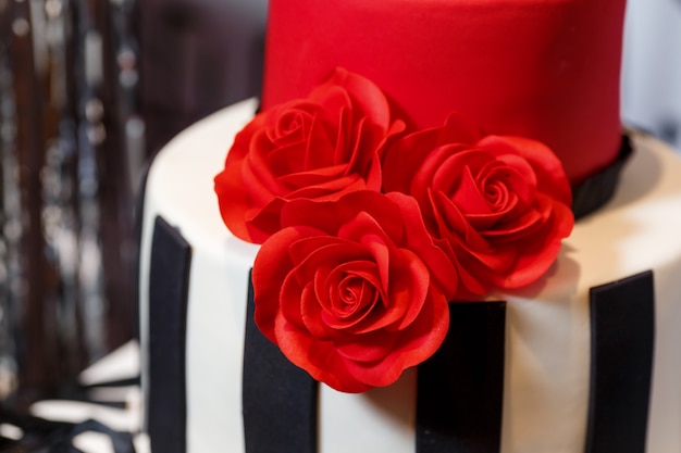 birthday party with beautiful big cake, decorated with roses and standing on barrel. Tasty sweets with cream decor in black, red, white colors