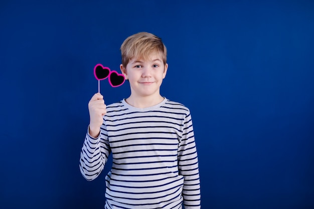 Birthday party and young boy with glasses in hats and props on blue wall