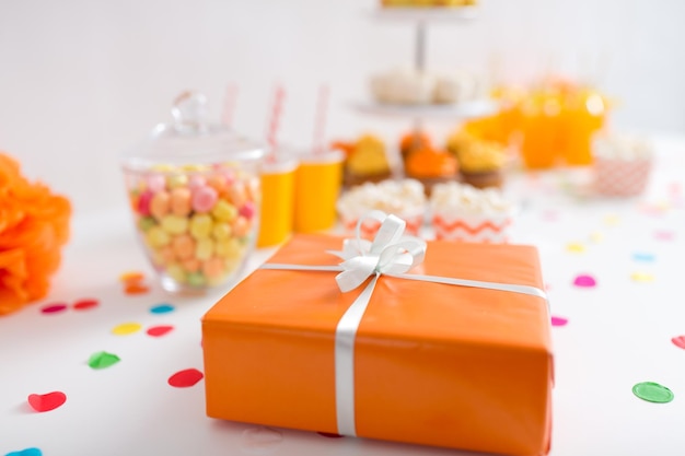 подарок на день рождения в оранжевой упаковке на столе на вечеринке