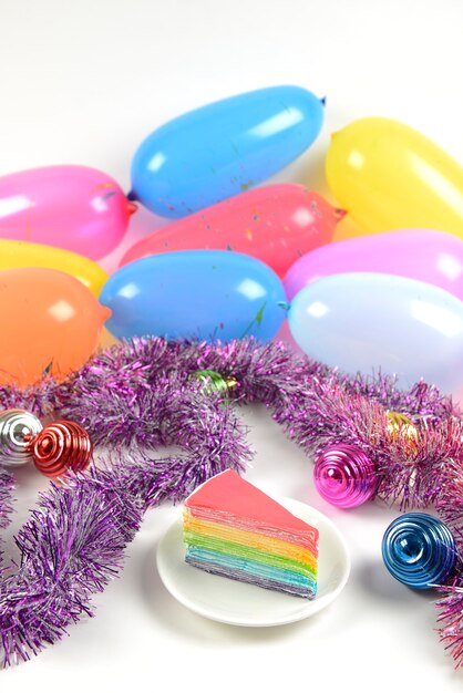 Birthday rainbow cake on party balloons background.