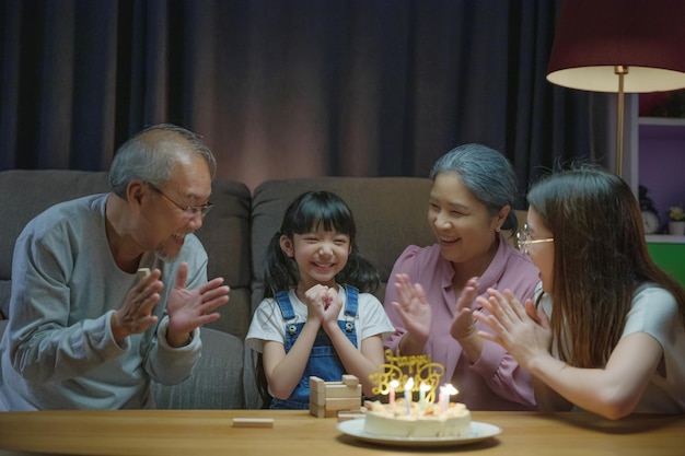 Сюрприз на день рождения. Счастливые азиатские семейные бабушка и дедушка и мать празднуют день рождения с тортом внучки дома в ночное время