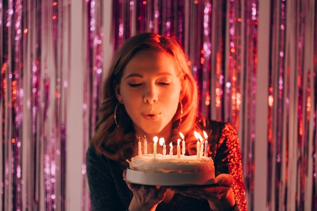 생일 소원 축제 여성 휴일 축하 반짝이는 보라색 캐스케이드 커튼 배경에 촛불을 불고 케이크를 들고 해피 레이디