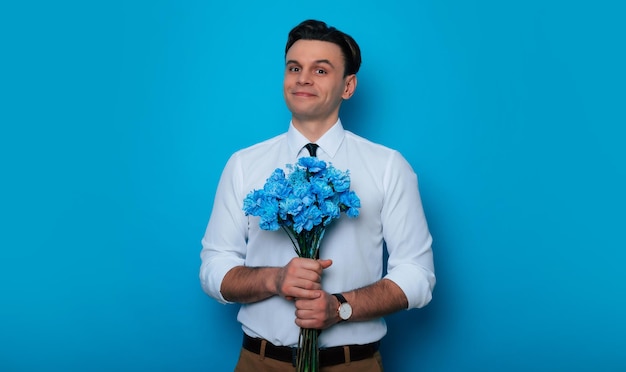 Birthday Women's Day Valentine's Day Holidays presents Excited handsome Smiling man in an elegant suit with a blue bouquet of flowers in hands looks at the camera on blue background isolated