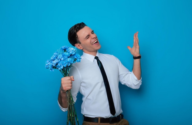 Birthday Womens Day Valentines Day Holidays presents Excited handsome Smiling man in an elegant suit with a blue bouquet of flowers in hands looks at the camera on blue background isolated
