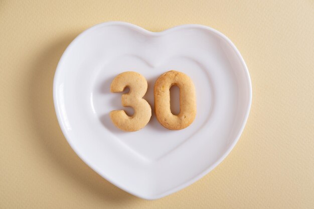 Photo biscuits forming number 30 on the white plate and yellow light background