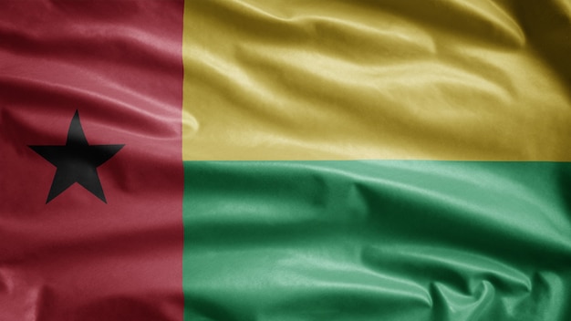 Bissau Guinean flag waving in the wind. Close up of Guinea Bisau banner blowing, soft and smooth silk. Cloth fabric texture ensign background. Use it for national day and country occasions concept.