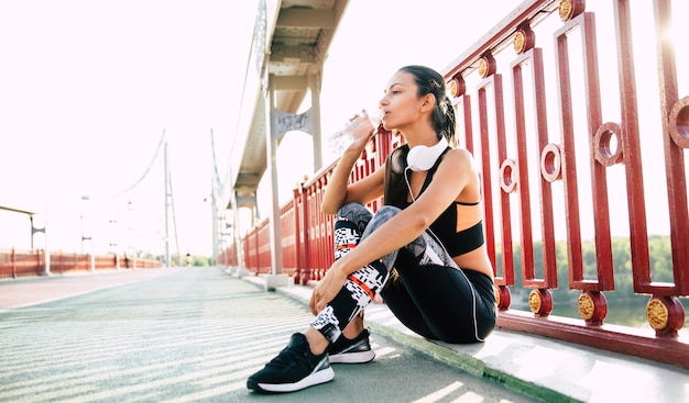 The bit of water during sport exercises. Woman is drinks water while resting after morning run