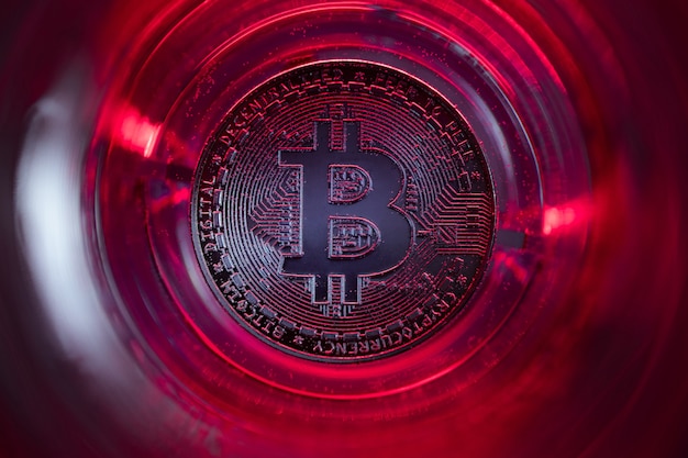 Bitcoin aan de onderkant van het glas met water en rode lichten. Close-up foto.