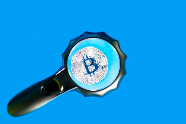 Bitcoin on a blue background through a magnifying glass