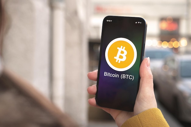 ビットコインBTC暗号通貨のシンボル、ロゴ。ビジネスと財務の概念。スマートフォンで手、暗号アイコンのクローズアップで画面