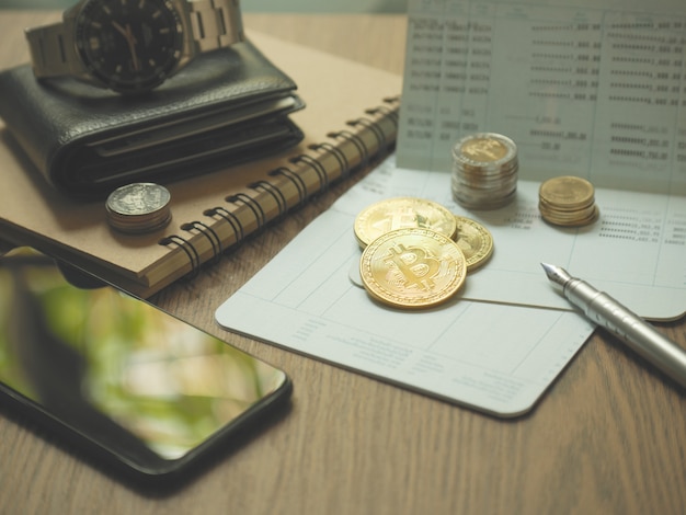 биткойн-монета и сберегательная книжка, ручка и смартфон на столе для бизнес-концепции