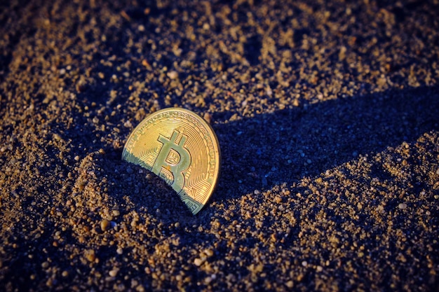 Bitcoin coin in sand at sunset collapse and fall cryptocurrency