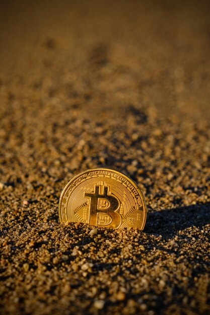 La moneta bitcoin nella sabbia al tramonto crolla e cade la criptovaluta