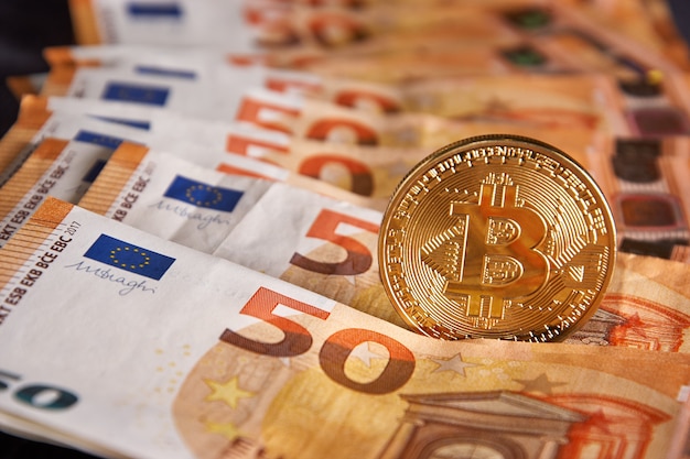 Foto bitcoin fysieke gouden munt op bankbiljetten van 50 eurobiljetten. bitcoin is een blockchain-cryptovaluta