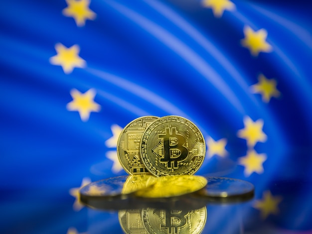 Bitcoin gold coin and defocused European flag background. Virtual cryptocurrency concept.