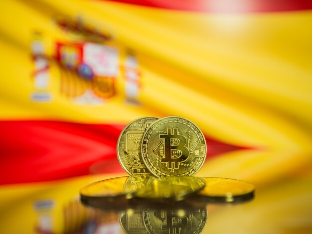 ビットコインゴールドコインとスペイン背景の焦点がぼけた旗。仮想暗号通貨の概念。