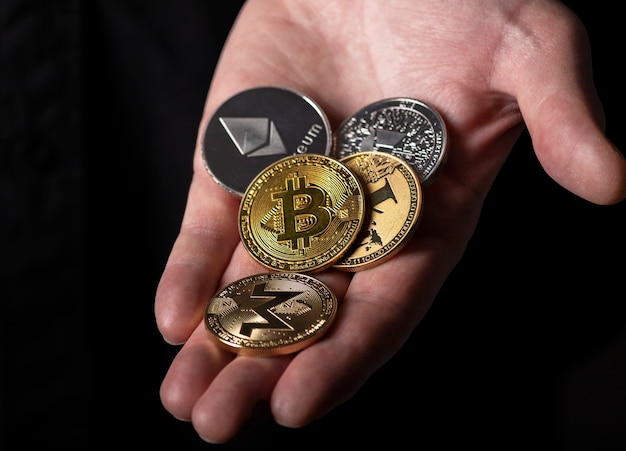 Photo bitcoin and other dofferent crypto currency coins in male hand palm over black background, close up.