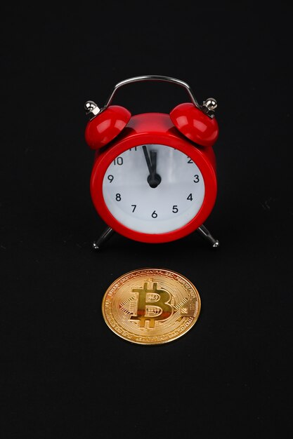 Bitcoin and red alarm clock on black background. Cryptocurrency concept. Gold Color coin.