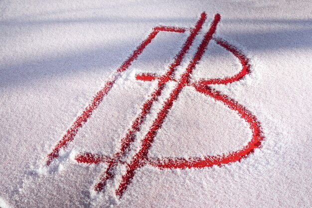 The bitcoin symbol is handwritten in the snow. Red metal is visible from under the snow