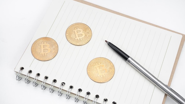 Bitcoin with pen on blank page notebook top view