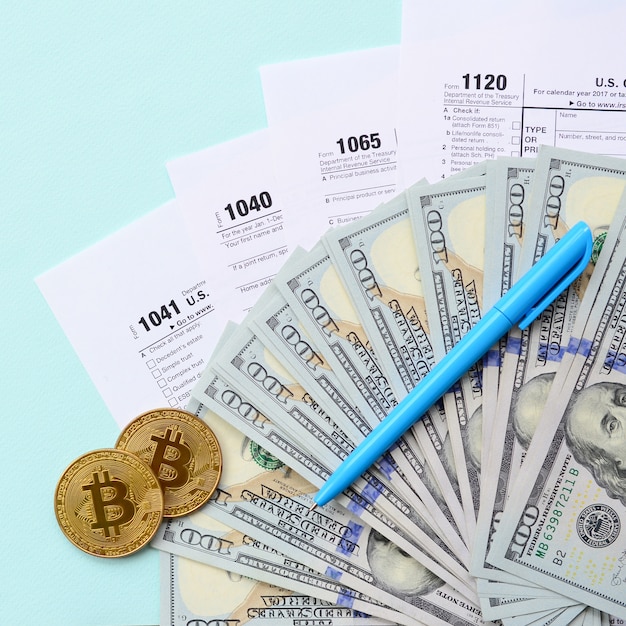 Bitcoin si trova con i moduli fiscali e centinaia di banconote da un dollaro su uno sfondo azzurro. dichiarazione dei redditi
