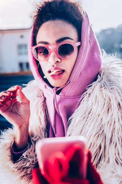 Bite it. Cheerful brunette female wearing glasses while doing selfie photo