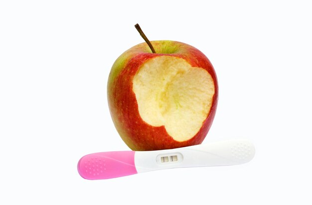 A bite out of apple and a pregnancy test on a white surface