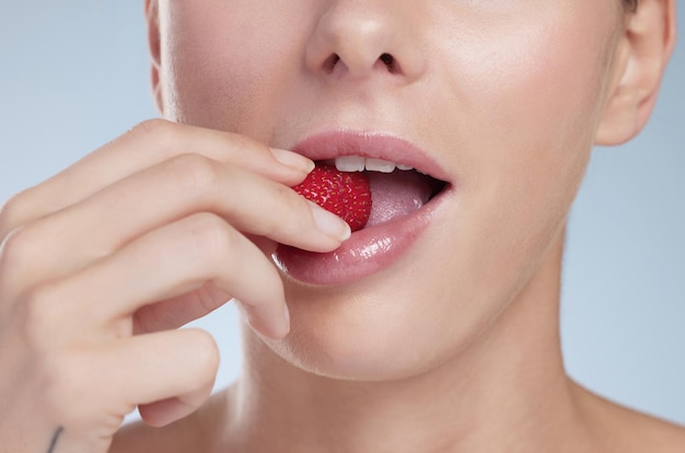 Biting into goodness Studio shot of an unrecognizable young woman biting into a strawberry against a grey background