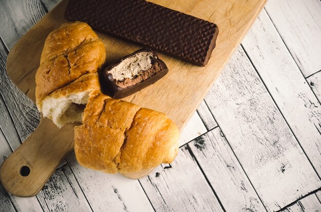 Bitten croissant and cakes on wooden table. 