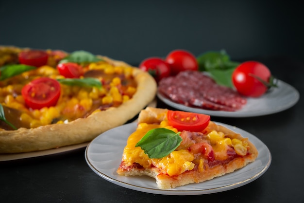 A bitten piece of pizza on a black background. Bitten piece of delicious Italian pizza on a dark background. Authentic national dish of Mediterranean cuisine.