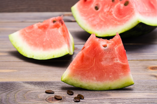 A bitten piece of watermelon and large pieces of watermelon on a wooden table