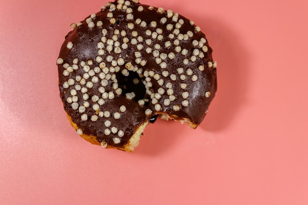 Bitten tasty chocolate donut on a pink background Top view