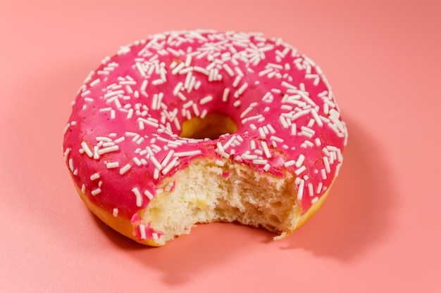 Укушенный вкусный розовый пончик на розовом фоне