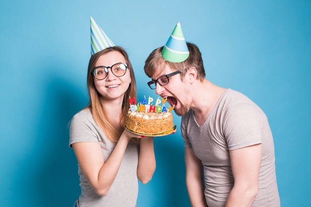 Bizar jong koppelmeisje en jongen met papieren hoeden willen een stuk felicitatietaart afbijten. Verjaardag en gefeliciteerd concept.