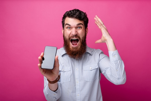 Blaas je geest concept. Jonge, bebaarde man met smartphone lege display, gebaren met zijn hand in de buurt van zijn hoofd.