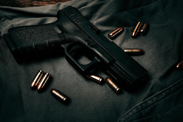 Black 9mm pistol on a black gray fabric background with 9mm ammunition next to it top view