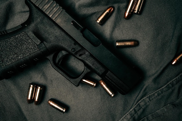 Black 9mm pistol on a black gray fabric background with 9mm ammunition next to it top view