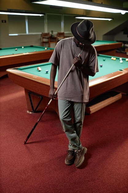 Black adult man wearing hat posing by pool table