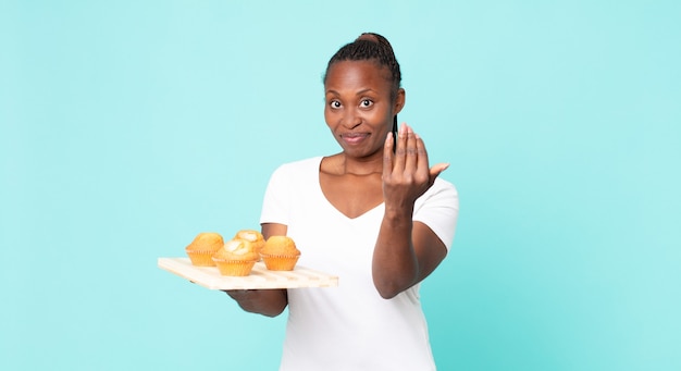 Photo black african american adult woman holding a muffins tray