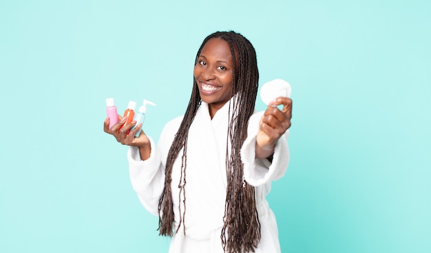 Black african american adult woman wearing bathrobe and holding cosmetic products